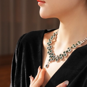 Silver V-shaped necklace with green emerald stones worn by a model in soft lighting