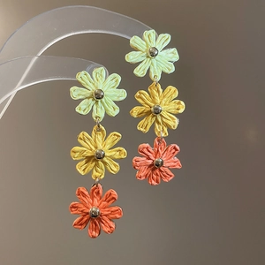 Macro detail of woven raffia flower drop earrings with yellow and orange color gradient