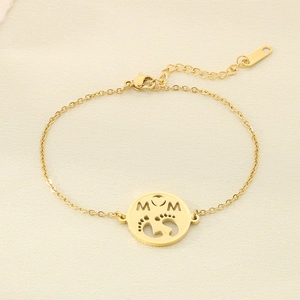 Detail of gold MAMA charm bracelet with openwork heart and baby footprints on fabric