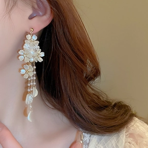 Elegant floral drop earrings with white petals and pearls worn by a model in a close-up view