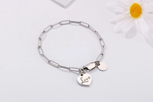 Macro shot of silver paperclip chain bracelet featuring engraved Love heart and round pendant
