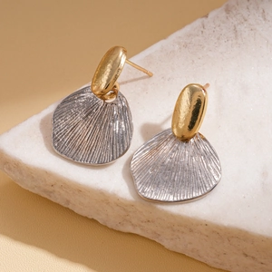 Detailed close-up of geometric gold and silver metallic earrings on white porous stone
