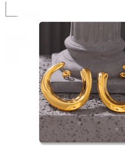 Close-up of chunky gold-plated U-shaped hoop earrings on a textured stone pedestal