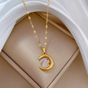 Macro view of gold moon necklace with white rabbit pendant on silk fabric background