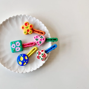 Five colorful geometric children hair clips in floral and heart shapes on a white tray