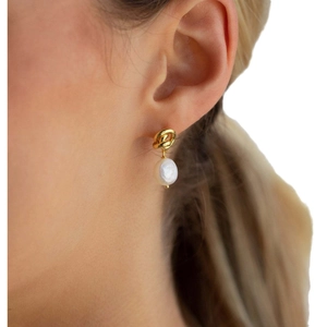 Golden knot earrings with baroque pearl pendants worn by a model in a professional close-up