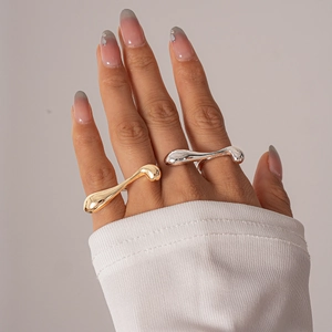Close-up of gold and silver irregular fluid rings worn by a model on a neutral background
