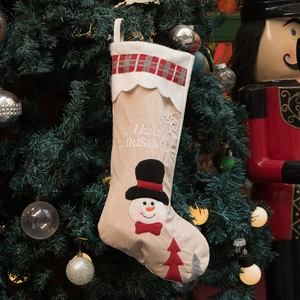 Rustic burlap Christmas stocking with snowman embroidery hanging on a festive Xmas tree