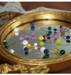 Detail of colorful round bead stud earrings in purple blue green and yellow on a gold tray