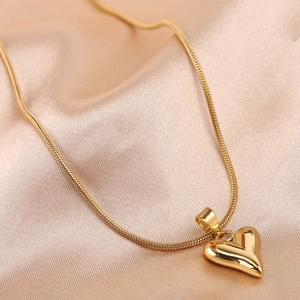Close-up of a polished golden heart pendant necklace on an elegant gold satin background