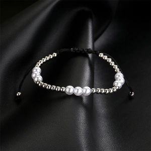 Detail of hand-woven bracelet with white faux pearls and silver beads on leather surface