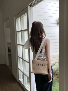 Detail of straw woven tote with PARIS embroidery and cream straps on a female model