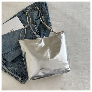 Chic silver tote bag with golden chain strap styled on a bed with a denim jacket