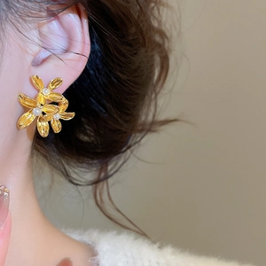 Macro detail of gold flower earrings with pearls shown on a person's ear