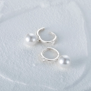 Detailed close-up of pearl drop earrings with cubic zirconia on textured stone background