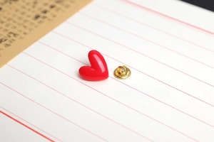 Detailed view of red heart enamel pin with golden butterfly clasp on white paper
