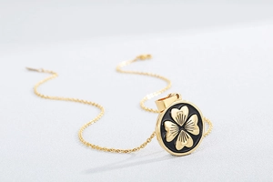 Macro shot of circular gold four-leaf clover pendant with black enamel on a fine chain