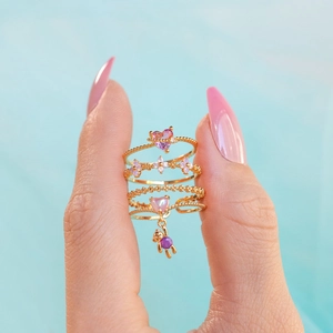 Close-up of a hand wearing four gold rings with colorful zircons on a light blue background