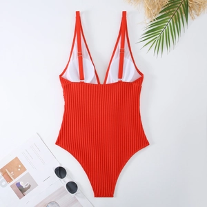 Dettaglio di un costume intero rosso a coste con scollo a V e foglie di palma sul fondo