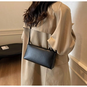 Minimalist black matte leather baguette bag worn crossbody over a beige trench coat