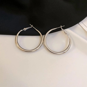 Dettaglio ravvicinato di orecchini a cerchio in argento lucido su sfondo minimalista bicolore