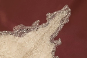 Close-up of fine floral lace trim and mesh fabric texture on an ivory satin skirt