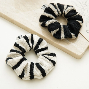 Detail of black and beige striped tweed knit scrunchies set on an elegant marble tray