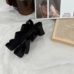 Detail of a large black satin bow banana clip on aesthetic wrinkled paper background