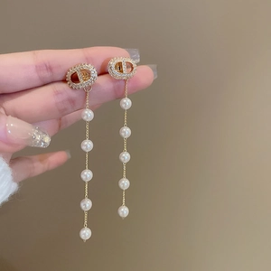 Detail of gold CD logo earrings with elegant long white pearl tassels held by hand