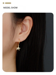 Close-up of gold starfish drop earrings with small diamonds worn by a model