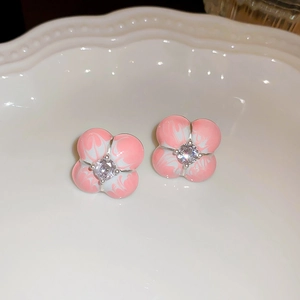 Close-up of pink enamel flower earrings with sparkling zircon center on a white plate