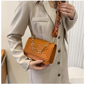 Detail of orange quilted crossbody bag with golden chain and retro woven strap