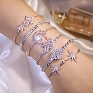 Close-up of gold and silver zircon bracelets with clover and swan charms on silk
