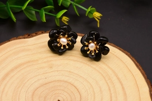 Macro detail of elegant floral pearl earring with black petals on natural wooden texture