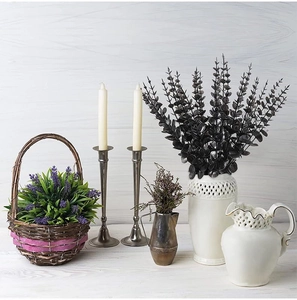 Black artificial eucalyptus leaves in a white vase with decorative candles and lavender