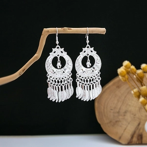 Ethnic bohemian silver tassel earrings with feathers hanging on a rustic wooden branch