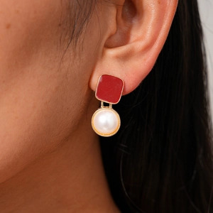 Gros plan de boucles d'oreilles géométriques en émail rouge et perle blanche sur modèle