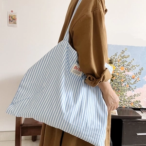 Grande borsa shopper in tela a righe bianche e blu indossata da una modella sulla spalla