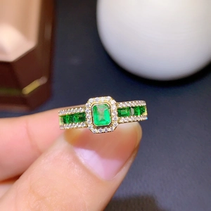 Luxury emerald-cut green gemstone ring in gold with diamond accents shown on finger