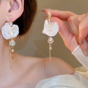 Close-up of white flower earrings with crystal beads and gold tassel chain on model