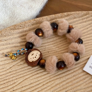 Détail du bracelet avec pendentif ours en bois et pompon sur un plateau beige