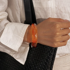 Close-up of translucent orange-red resin bangle with natural amber texture on wrist