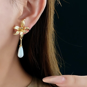 Detail of 14K gold plated floral earring with a white teardrop pearl on a model