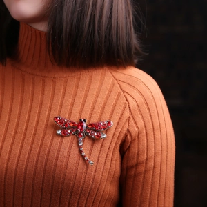 Vintage dragonfly brooch with red crystals pinned on a vibrant orange sweater