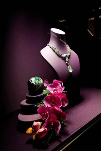 Detailed close-up of emerald and opal jewelry set on a professional purple display stand