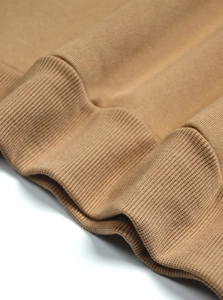 Macro shot of tan knit sweater cuff showing textured ribbed fabric and premium stitching