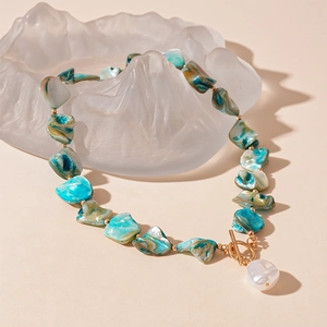 Dettaglio della collana di perle blu-verdi con chiusura a T dorata e perla barocca