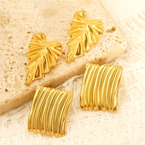 Detail showing gold leaf-shaped and textured rectangular earrings on a stone display