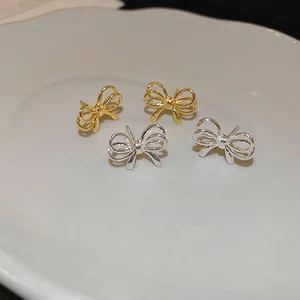 Elegant minimalist metal bow stud earrings in gold and silver finish on white porcelain