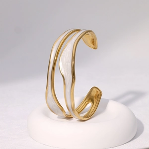 Detailed close-up of a gold-plated irregular bracelet with white enamel on a white ring stand